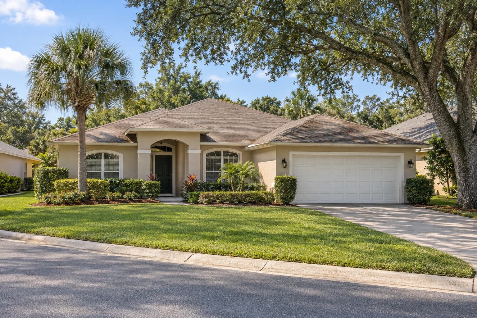 One-story 1990s stucco home with a hip shingle roof, white garage door, and a sabal palm and live oak on a quiet Citrus Park street