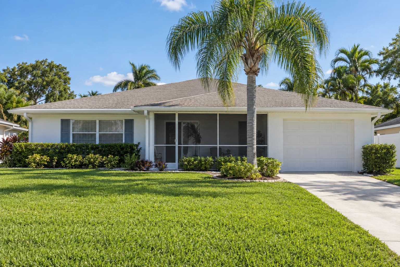 A one-story white-painted block ranch home in Seminole with a low hip roof, a screened porch, a queen palm, and a grassy yard on a quiet street