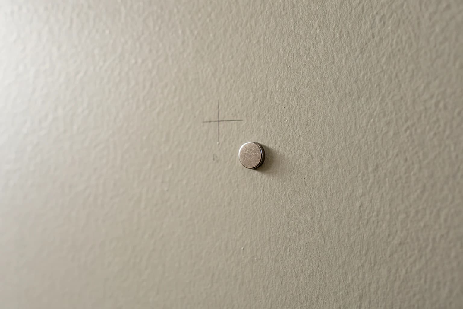 Close-up of a small strong magnet clinging to a painted drywall surface over a hidden screw head in a Florida home wall