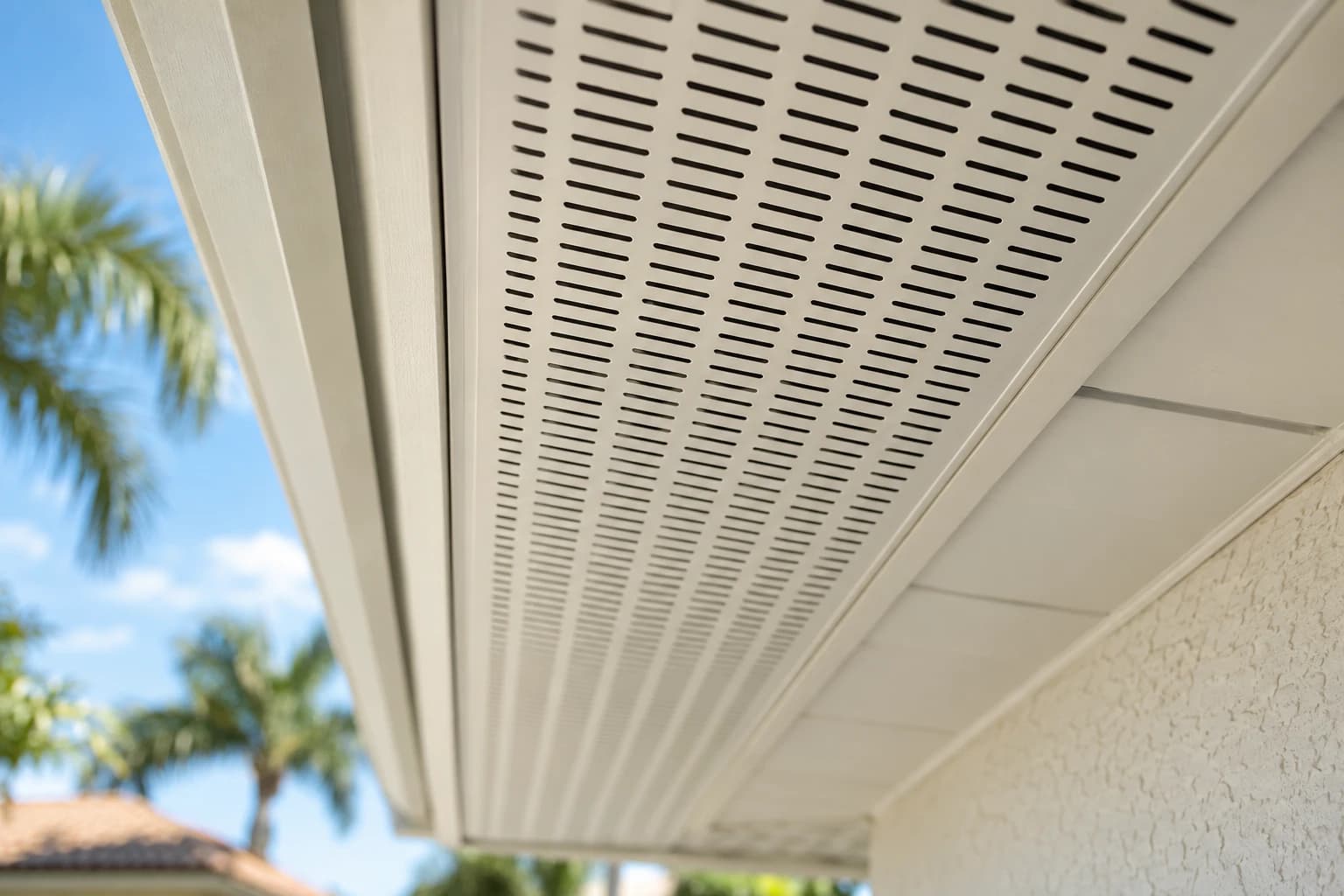 Open perforations in a continuous aluminum soffit vent seen from below, with daylight through the slots