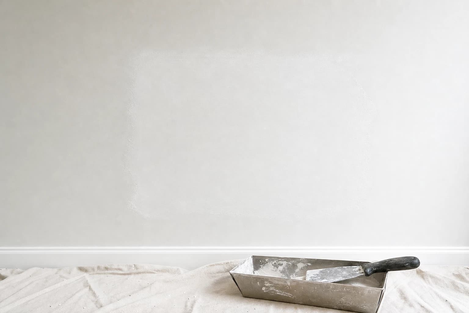 Rectangular drywall patch on a smooth Florida interior wall with joint compound feathered over mesh and a putty knife in a mud pan on the drop cloth