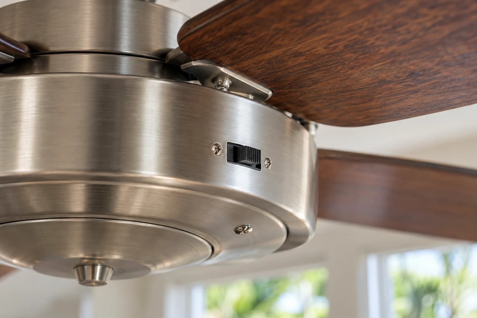Close-up of a small slide reverse switch on the side of a ceiling fan motor housing below still blades