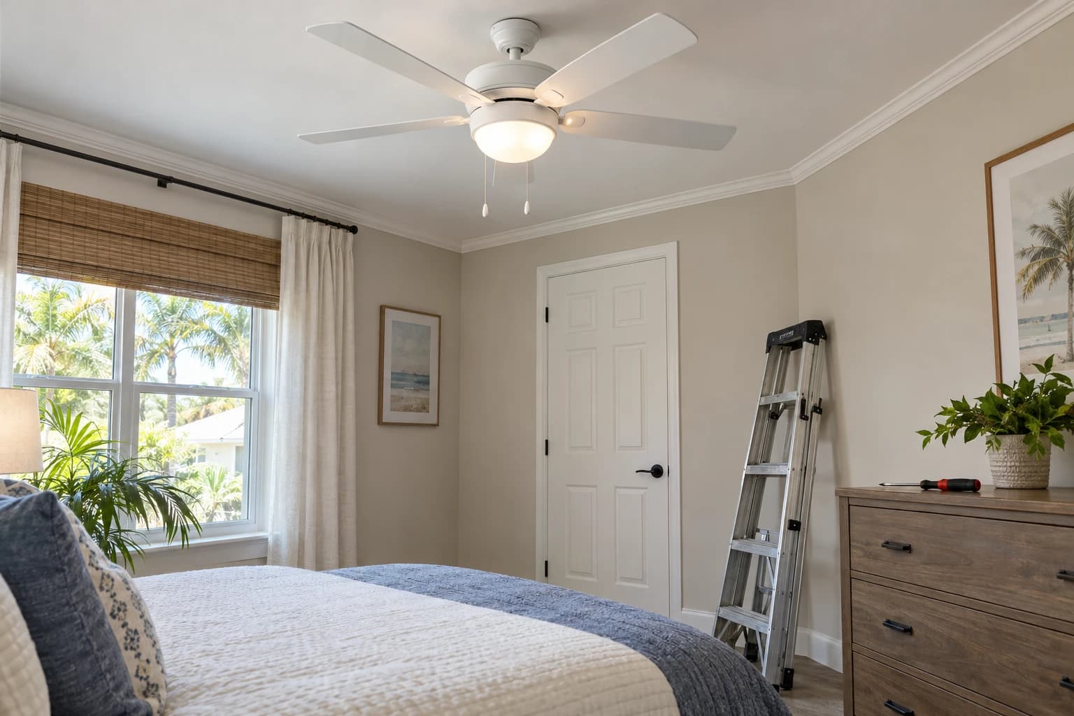 Bedroom ceiling with a new white five-blade ceiling fan and light kit, a stepladder folded against the wall and a screwdriver resting on the dresser