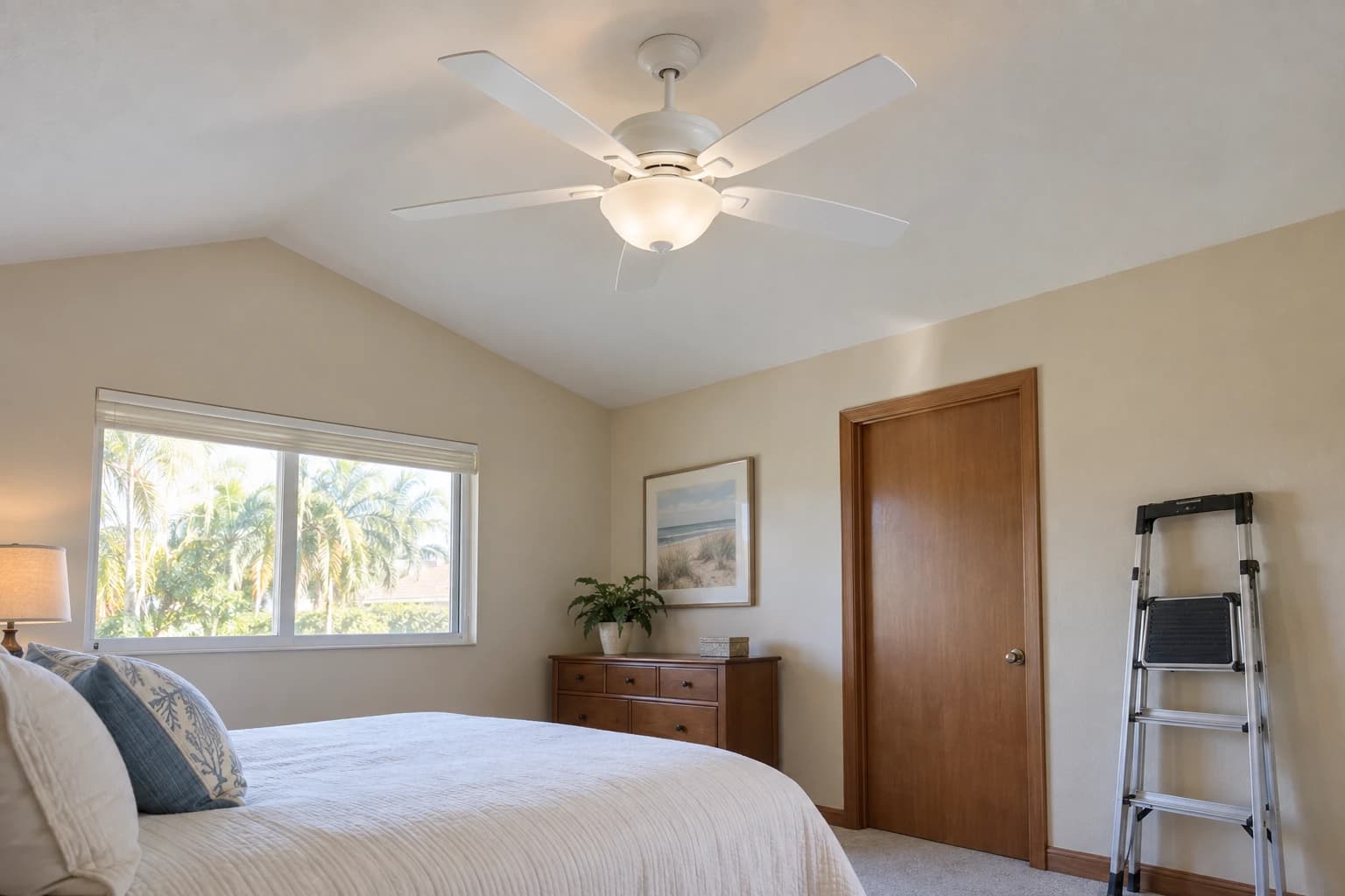 A new white five-blade ceiling fan with a frosted light kit in a bedroom with a vaulted ceiling, a stepladder folded against the wall
