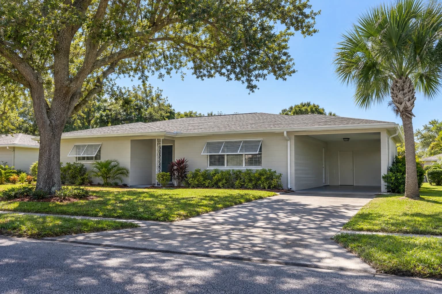 A one-story 1960s ranch house in Largo with painted block walls, a low hip roof, a carport, and a mature oak and palm in a green front yard