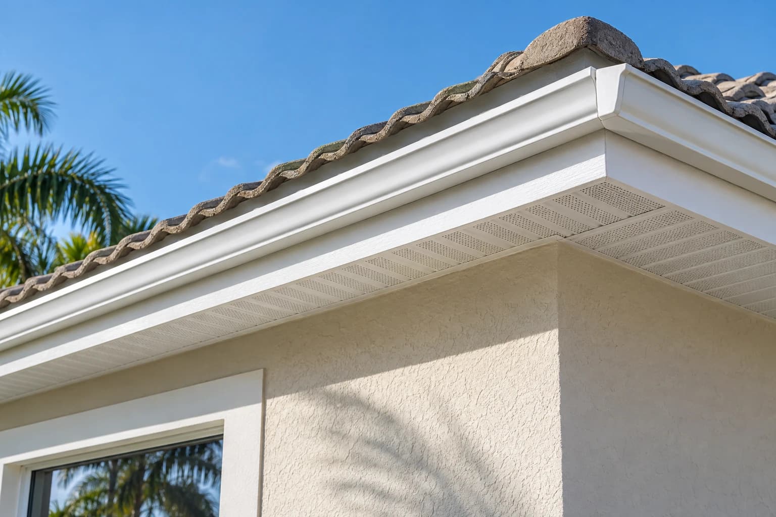New white fascia board and vented soffit panels under the edge of a tile roof on a stucco home, freshly painted