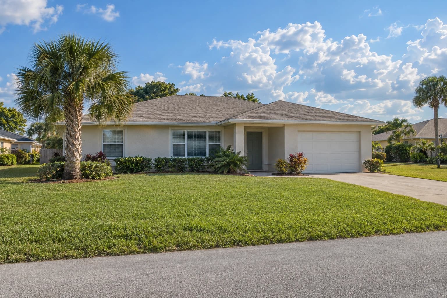 One-story concrete block home with pale stucco, a low hip roof, a single palm, and a wide green lawn on a quiet Palm Bay street