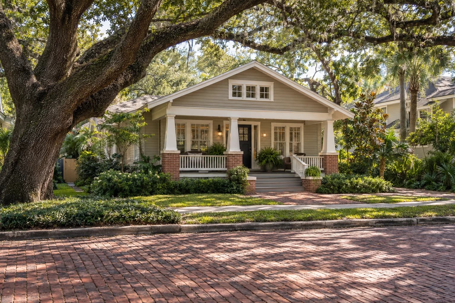 1920s craftsman bungalow with a deep front porch and tapered columns on a red brick street under arching live oaks in Palma Ceia