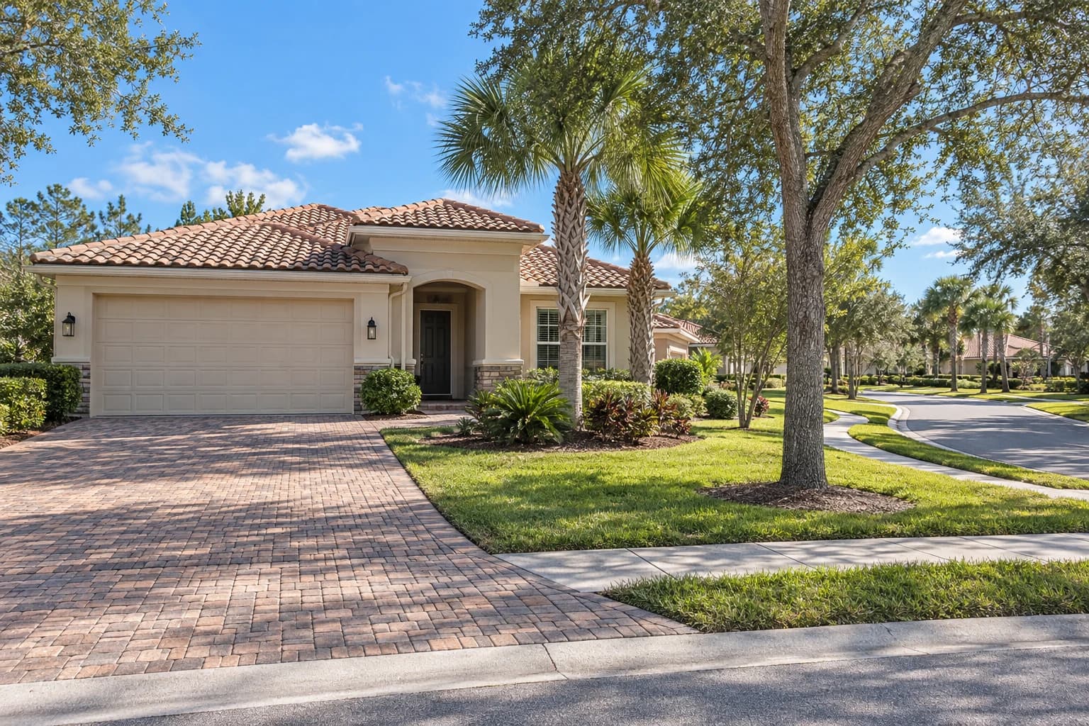 Newer one-story stucco home with a tile roof, a paver driveway, and young palms and live oaks along a quiet curving street near World Golf Village in St. Augustine