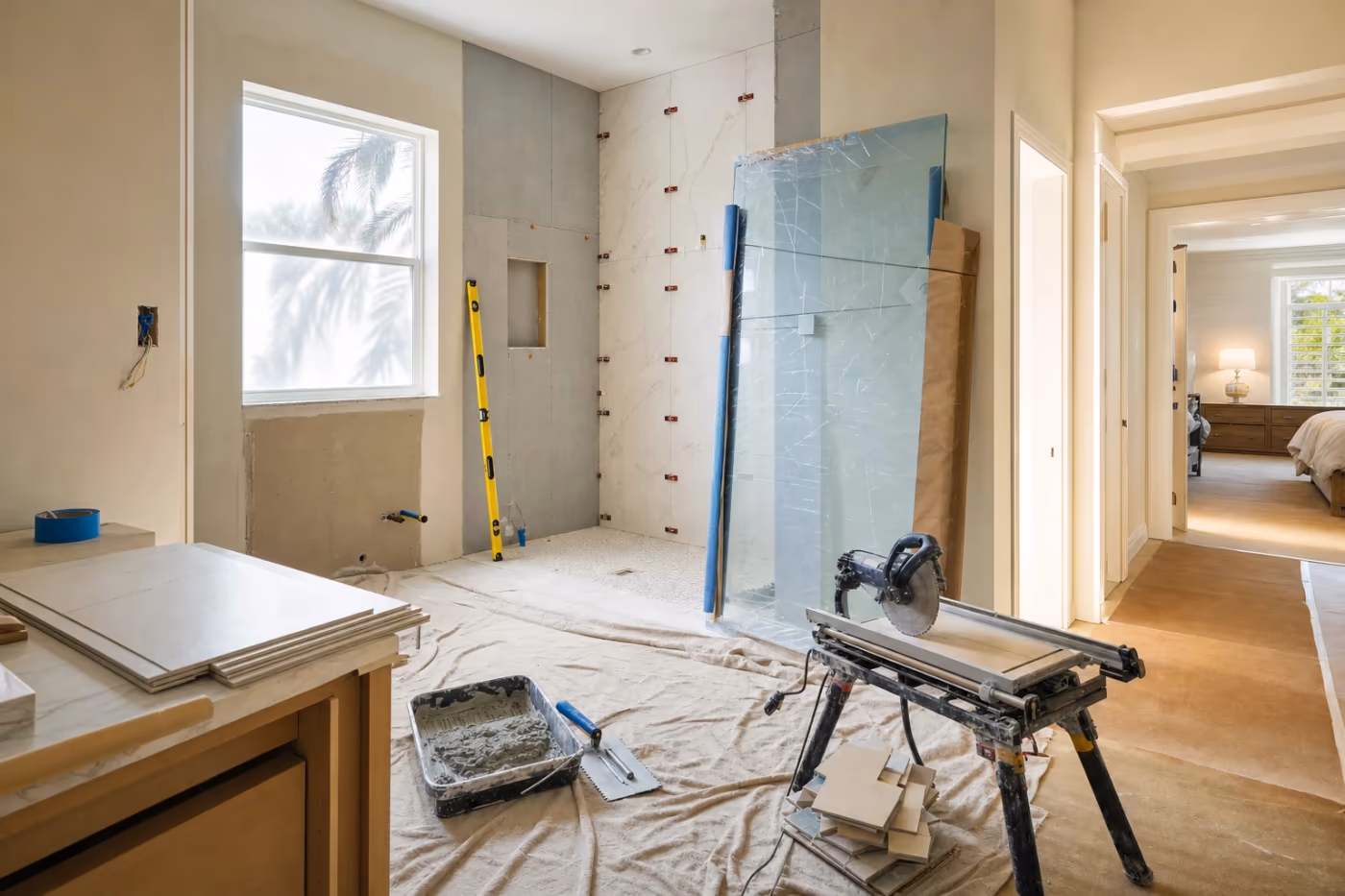 Mid-remodel Florida bathroom with tile staged, vanity prep underway, and professional tools set aside on drop cloths