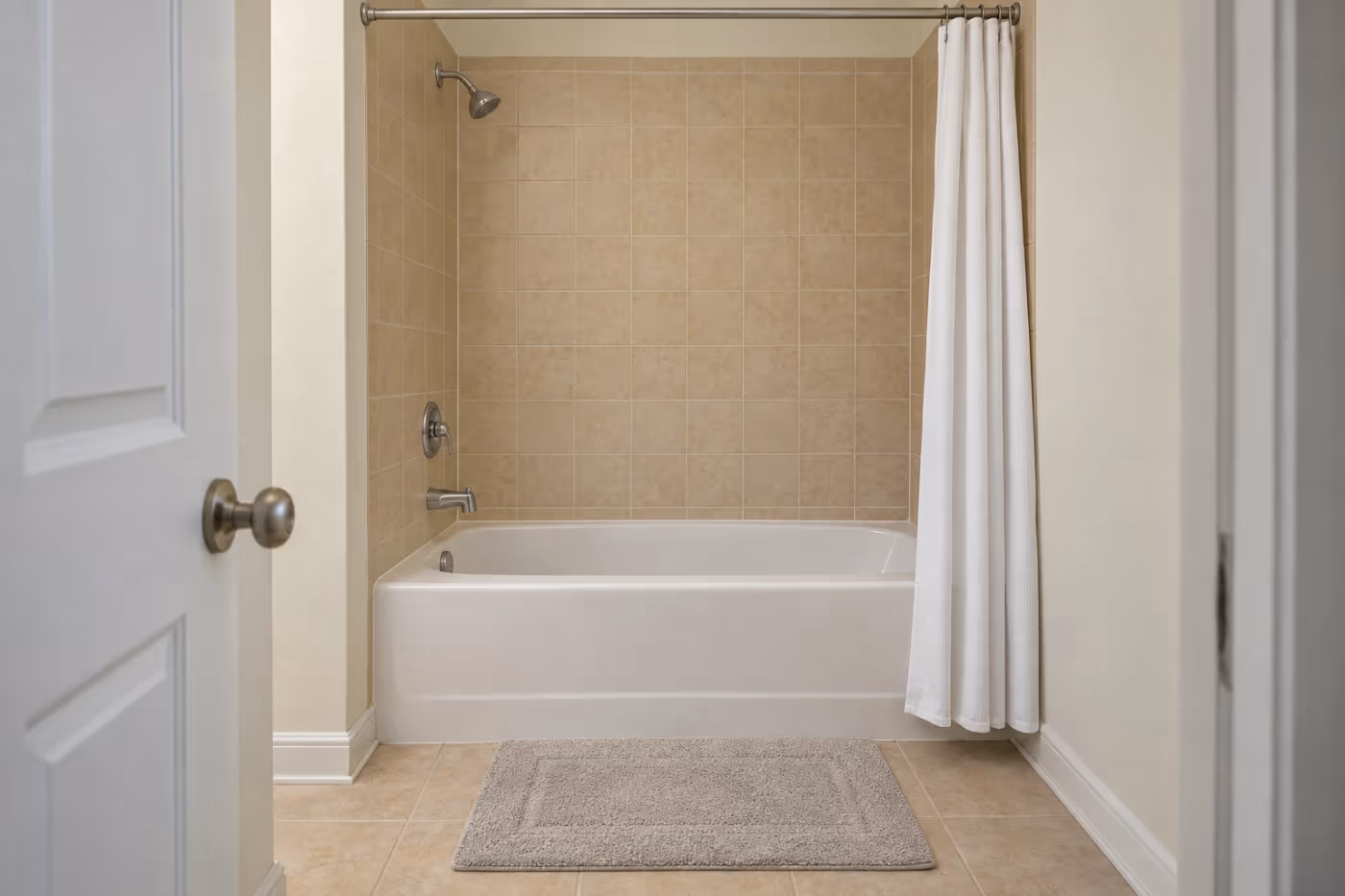 A dated Florida hall bathroom with a white builder-grade alcove bathtub, beige square tile on the walls above it, a chrome tub spout and shower head, and a shower curtain pushed to one side