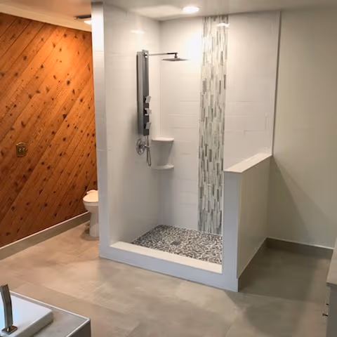 New tiled shower with a glass mosaic accent column and pebble floor, built by The Handyman Company