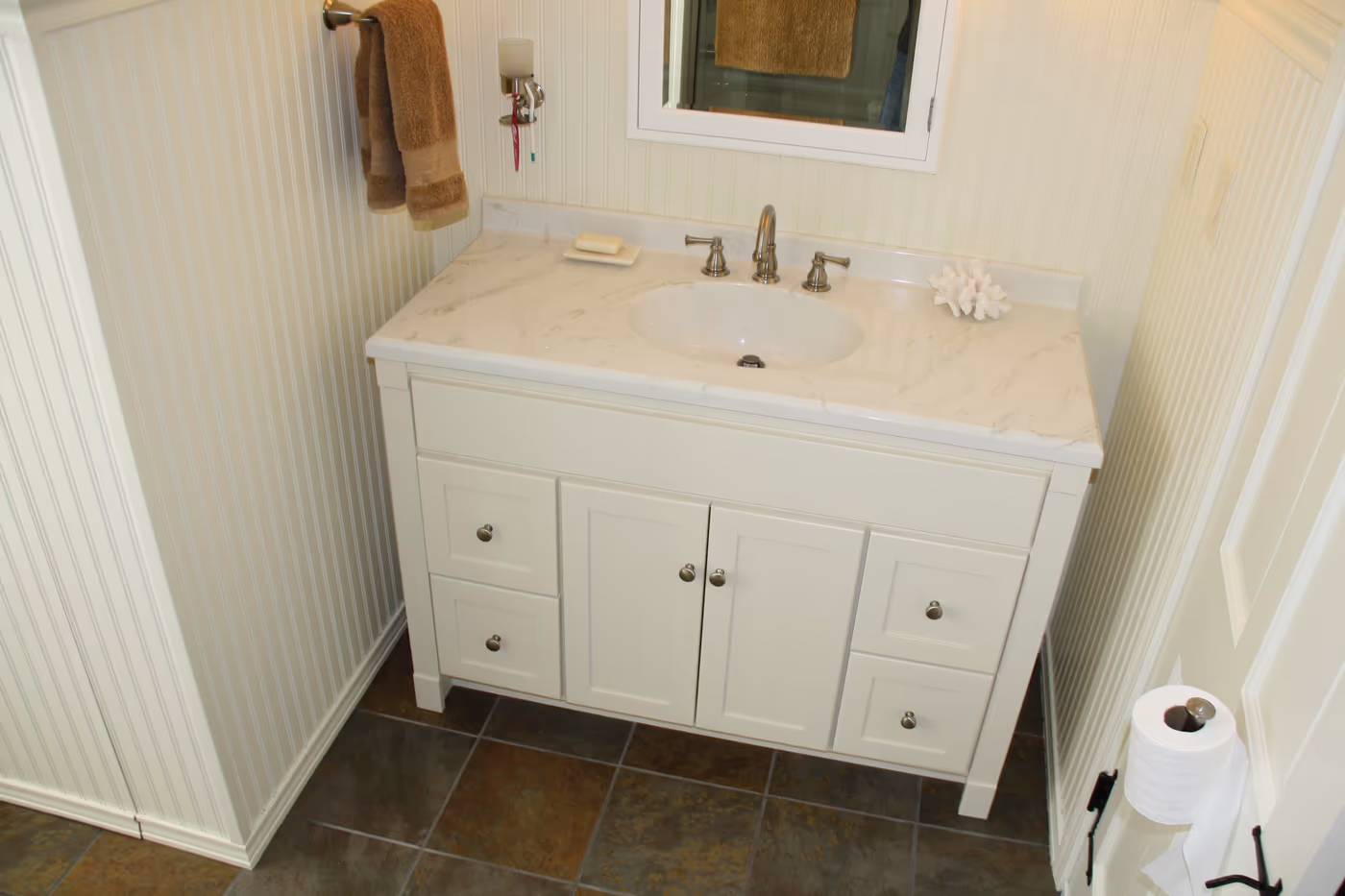 White shaker vanity with a marble-look top and a widespread faucet, set against beadboard walls over a slate tile floor