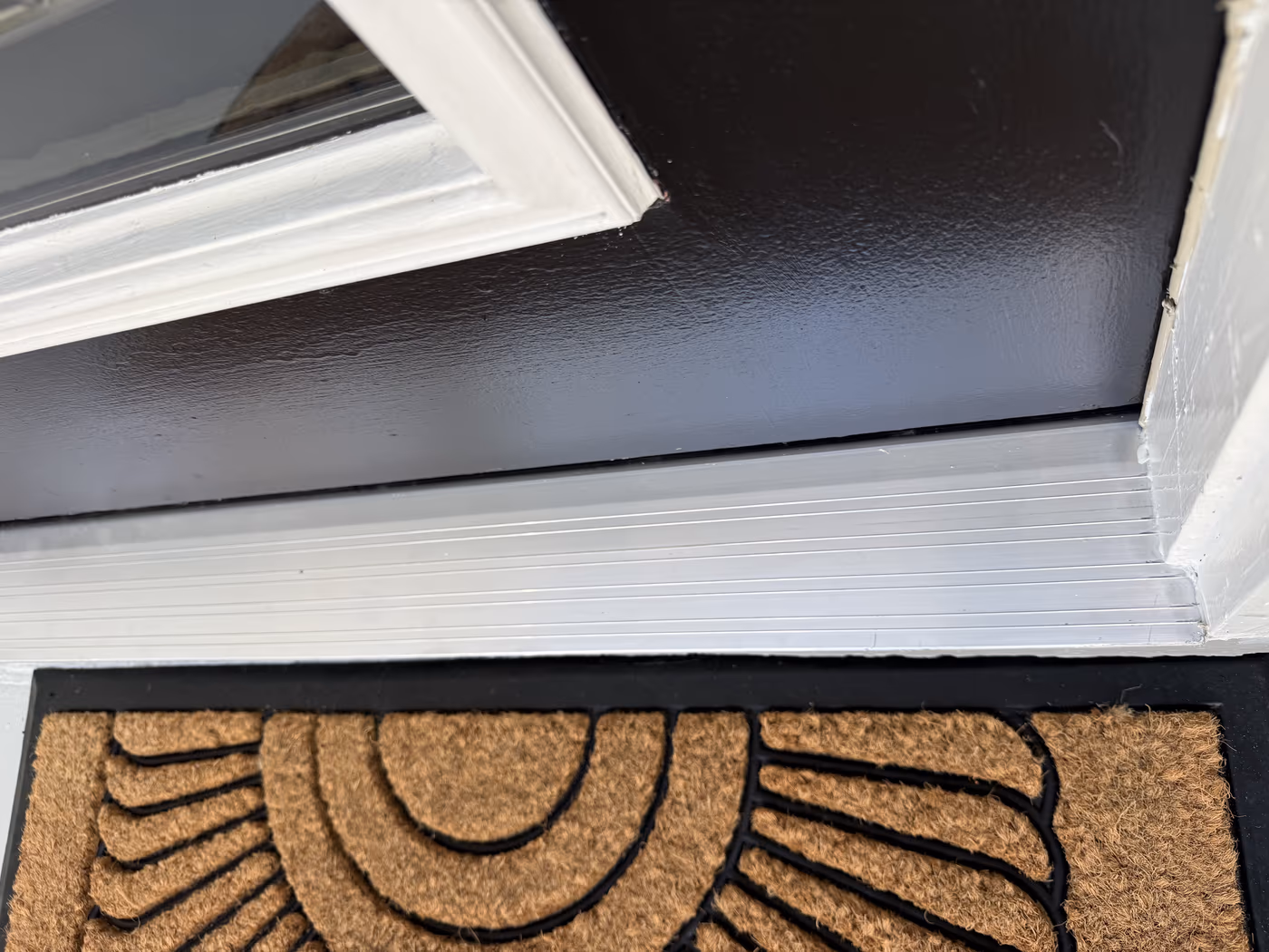 Close view of a new aluminum threshold under a dark painted entry door with white trim and a coir doormat