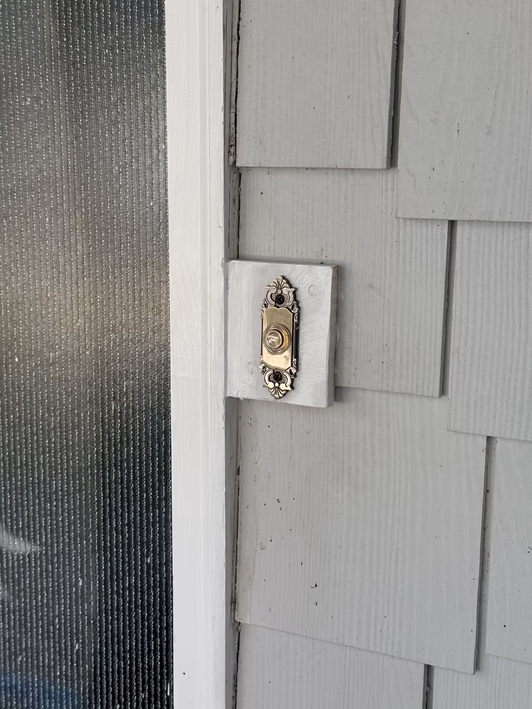 New lighted doorbell button mounted on painted shingle siding beside a front door