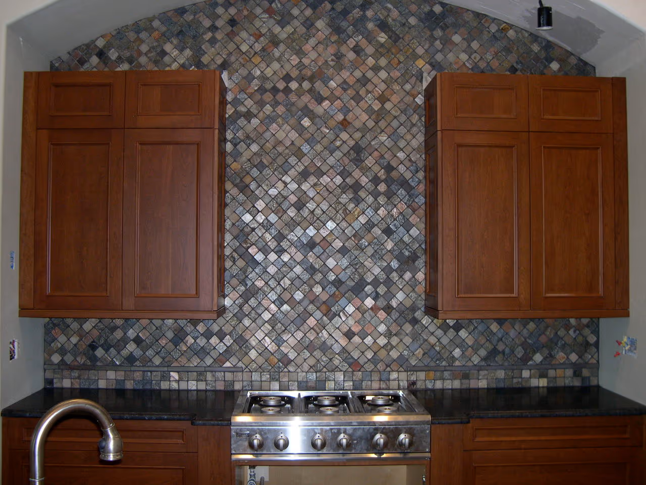 Full-height slate mosaic backsplash behind a stainless gas range