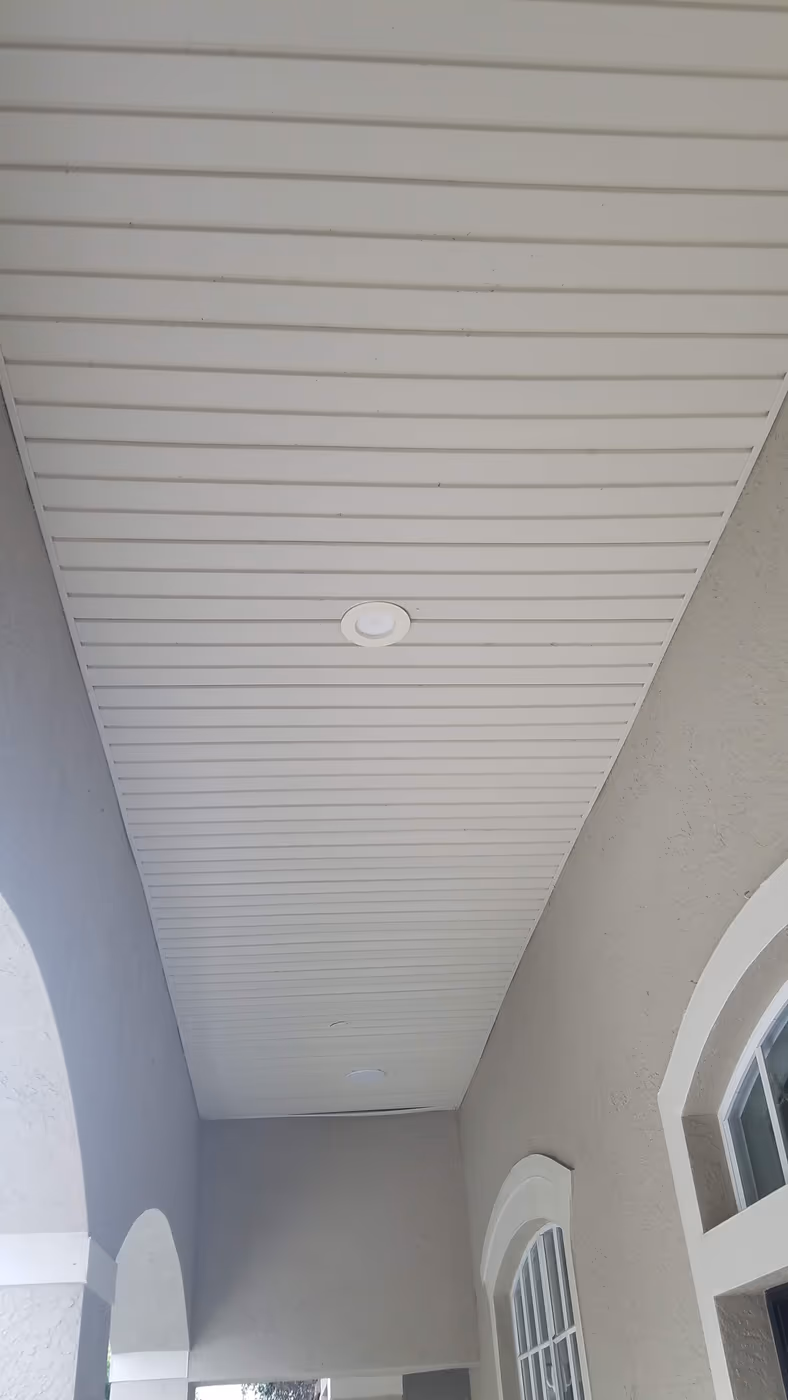 Covered porch ceiling finished in white beadboard with a recessed light, between arched stucco openings