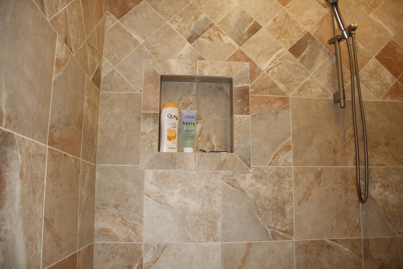 Shower wall with stone-look tile, a framed niche, and handheld shower