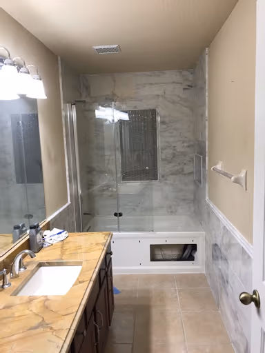 Small bathroom remodeled with marble-look walls and a glass tub enclosure