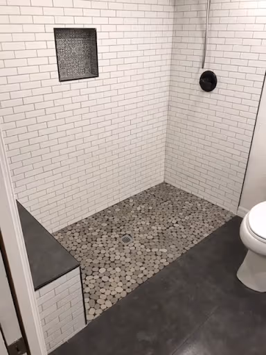 Walk-in shower with white subway tile, a tiled bench, and pebble floor