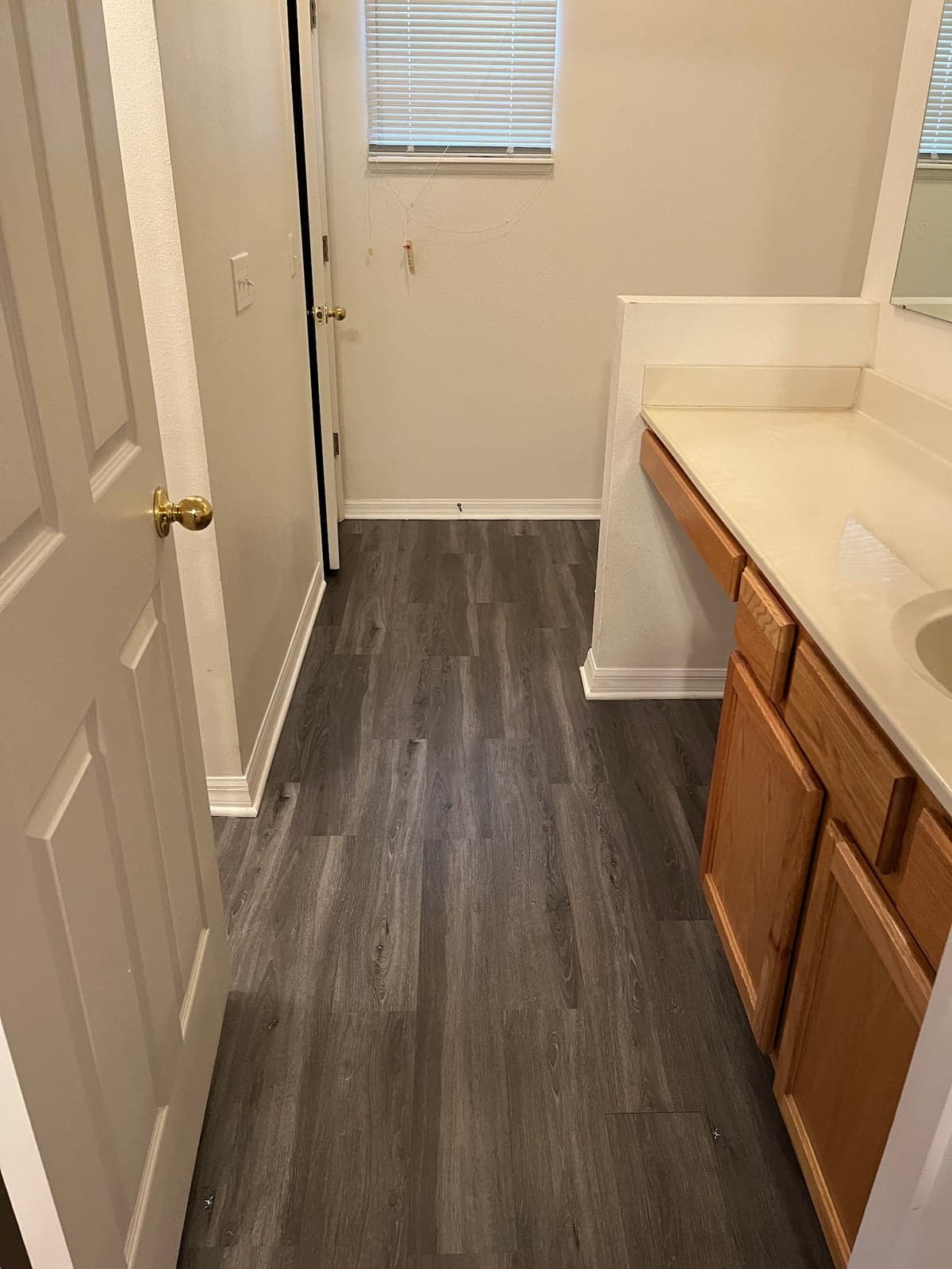 Gray wood-look plank floor running through a bathroom past an oak vanity and into a closet, with white baseboards