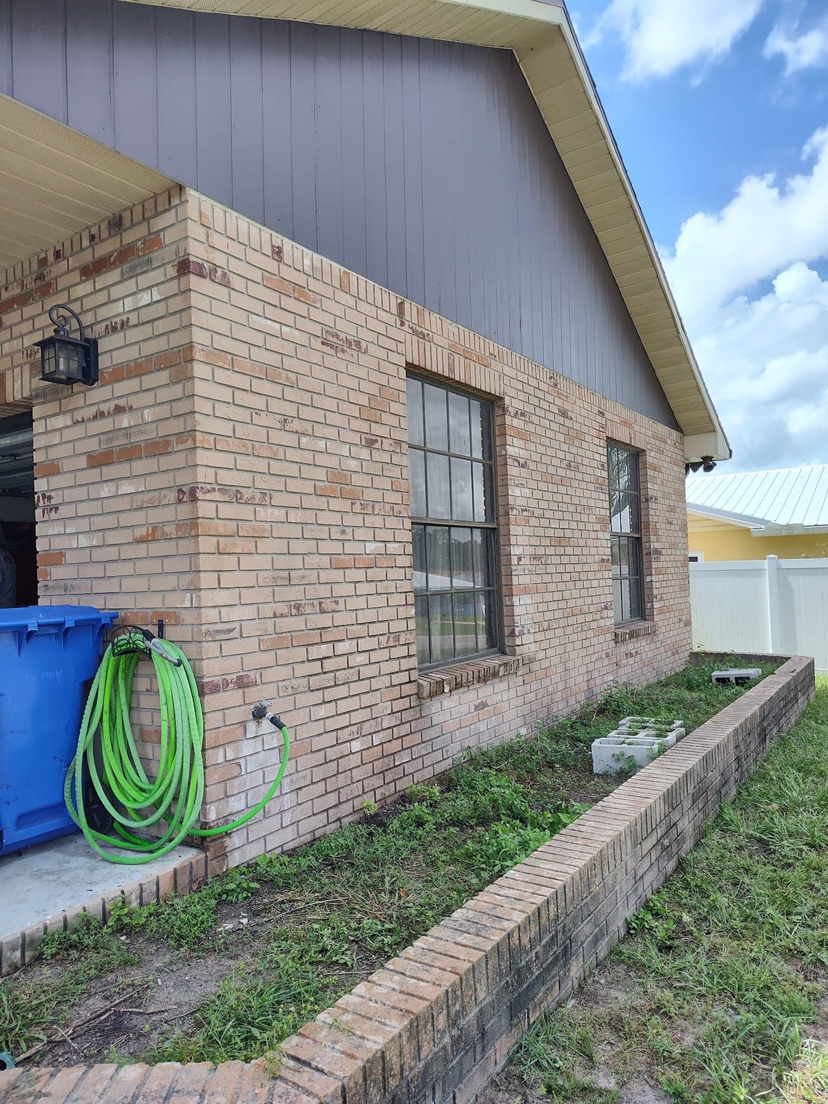 Tan brick house with a freshly painted gray siding gable end above two windows and a brick planter bed