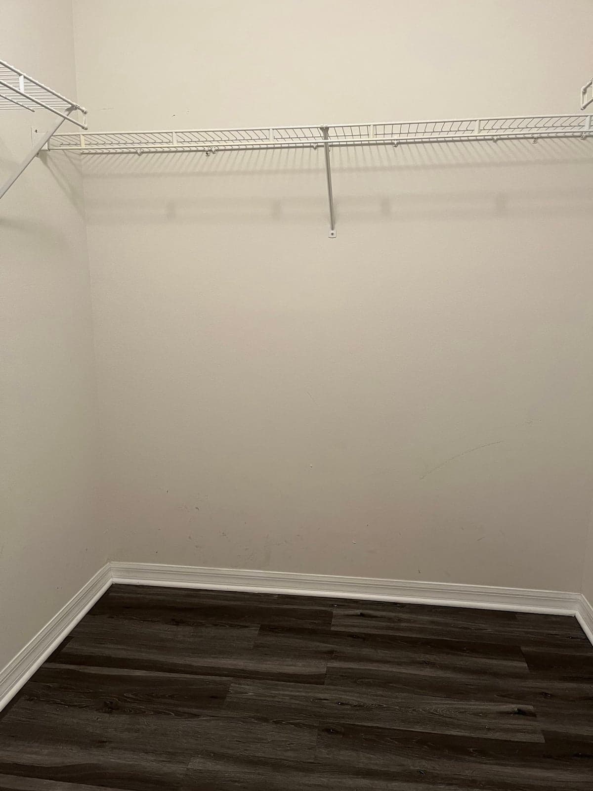 Empty walk-in closet with dark gray wood-look plank flooring, new white baseboard, and wire shelving on the walls