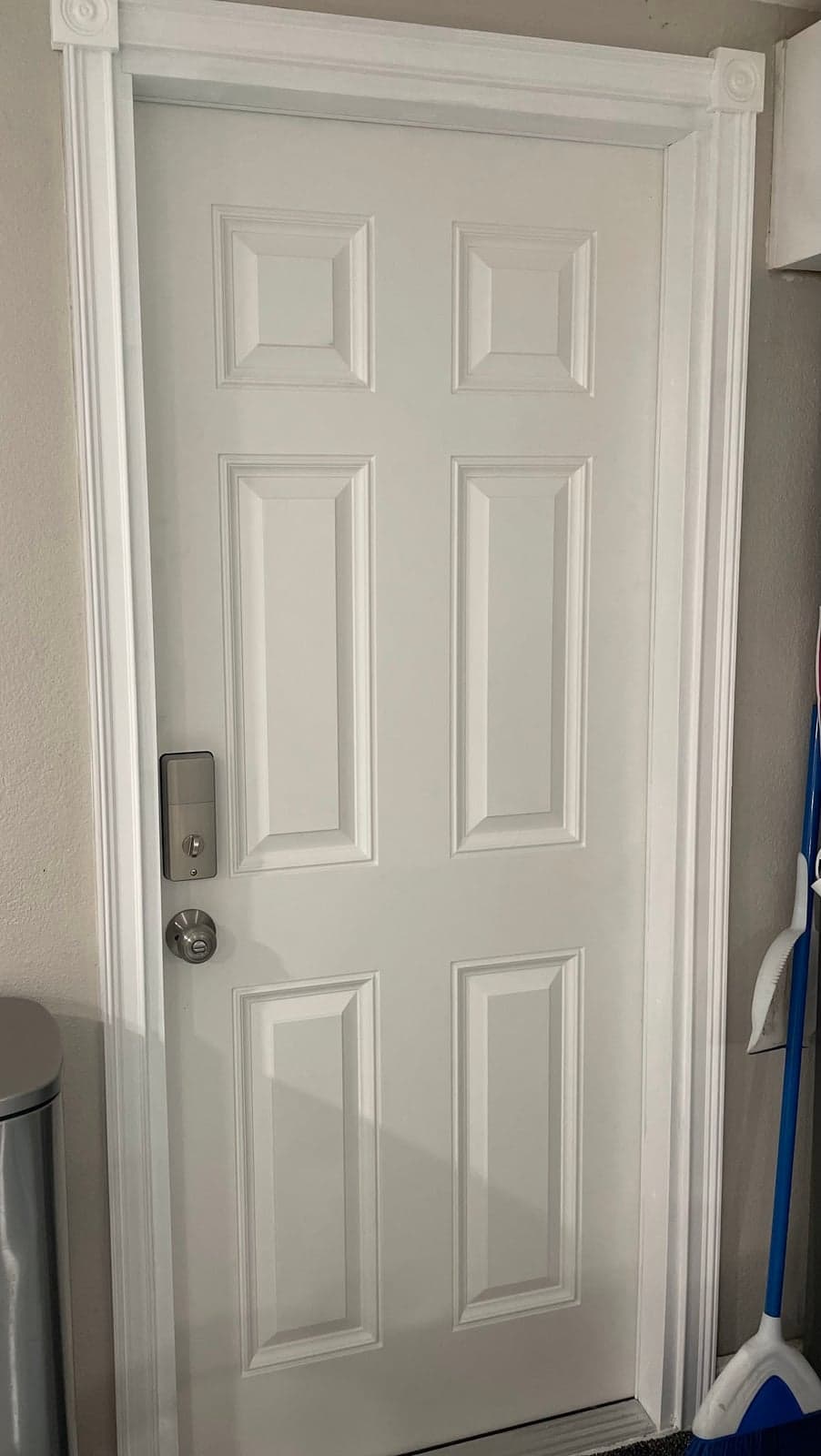 New white six-panel door with fluted casing, rosette corner blocks, a keypad deadbolt, and a brushed nickel knob
