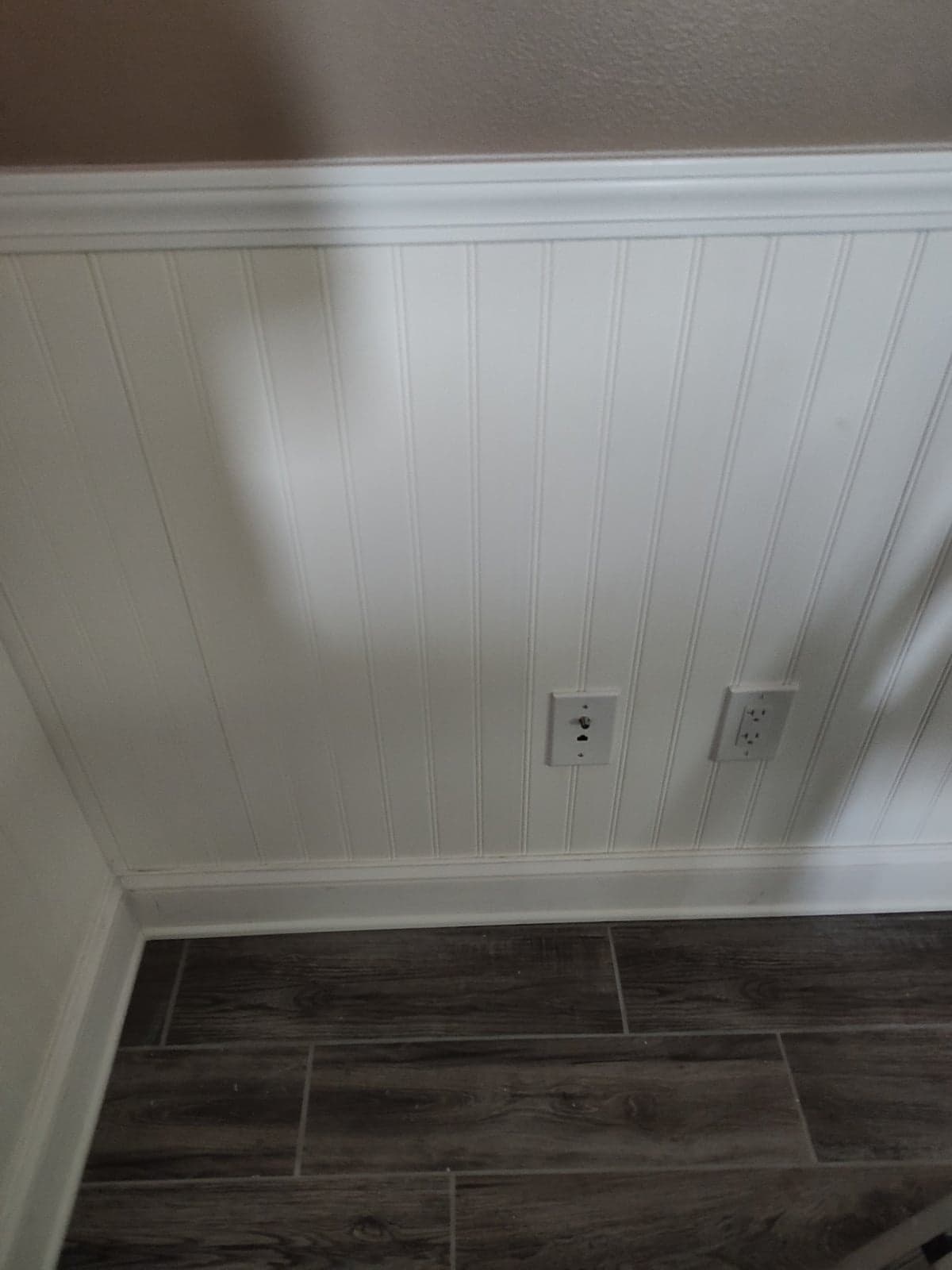 White beadboard wainscoting with a cap rail and new baseboard meeting a wood-look plank tile floor