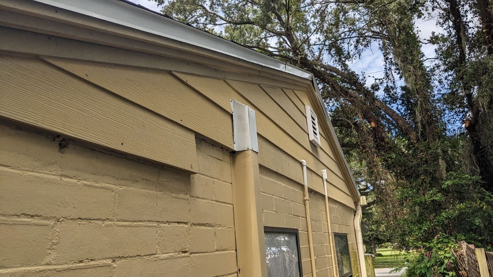 Gable end of an older home with new tan lap siding and trim under a clear sky with oak trees behind