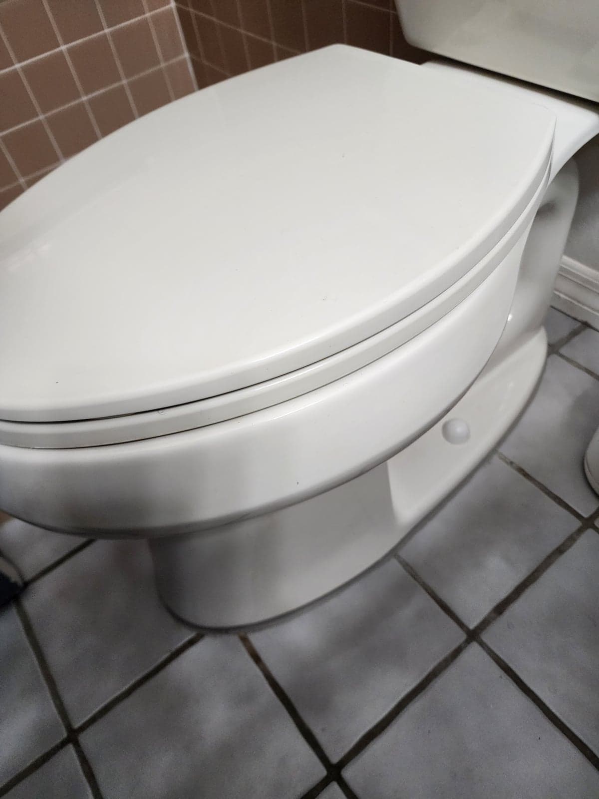 A white toilet sitting clean and level on gray tile after our team reset it on a new seal at the base