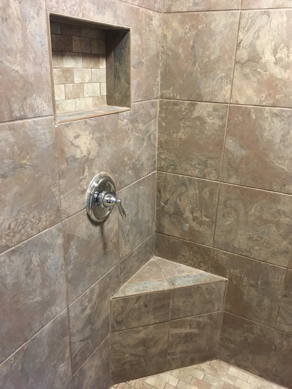 Tiled shower with large stone-look wall tile, a recessed niche, a corner bench, and a chrome valve handle