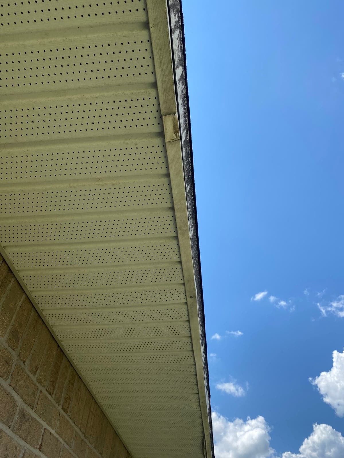 Looking up at rows of vented white soffit panels along the eave of a brick home against a blue sky