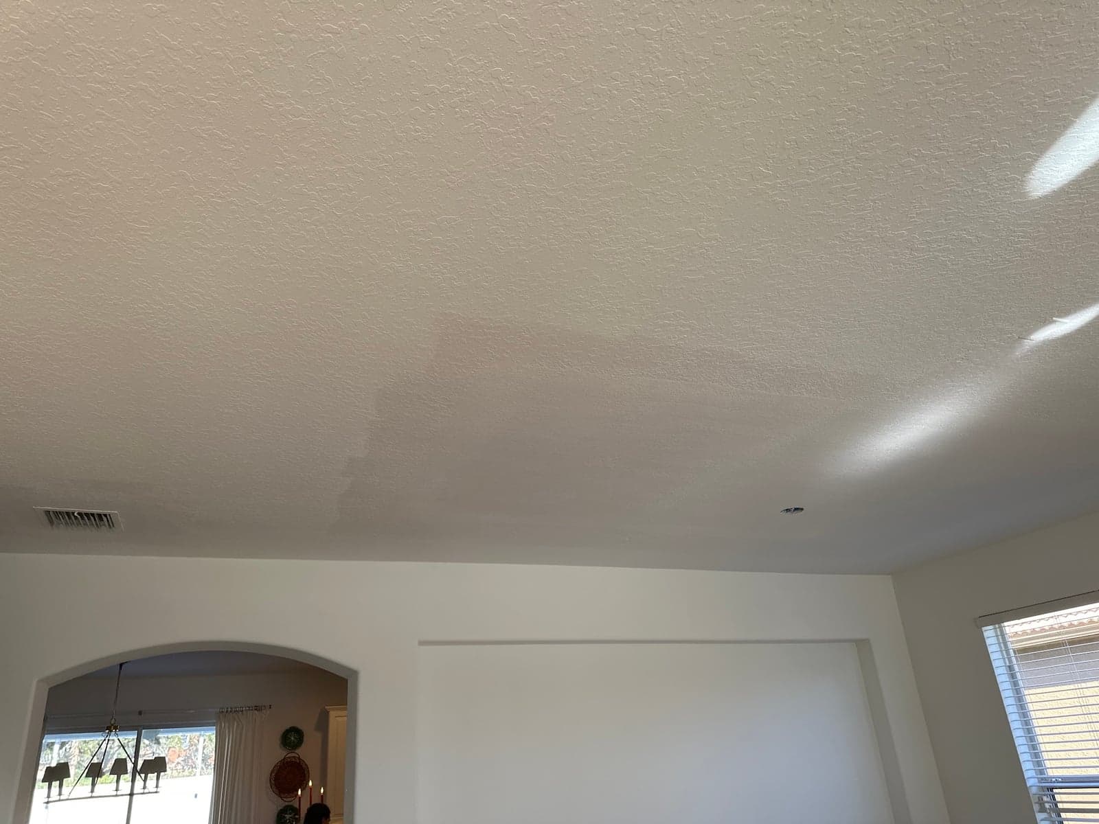 Textured white living room ceiling with a patched and painted section blending into the rest, above an arched opening and a window with blinds